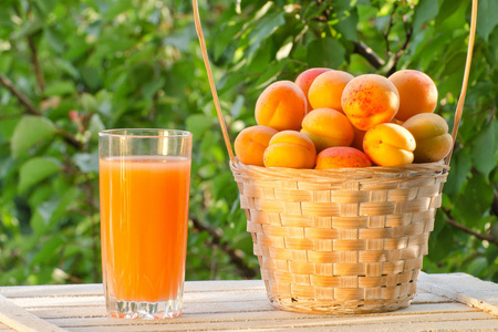 杏子在柳条篮子和一杯果汁的绿色背景，阳光