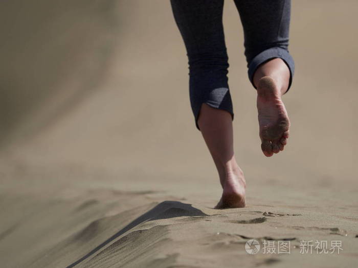 年轻女子跑步步行在日出海滩上赤裸的双脚