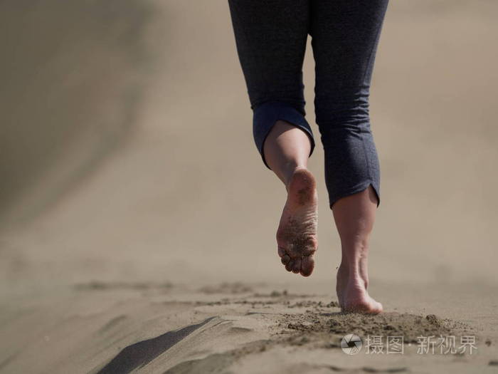 年轻女子跑步步行在日出海滩上赤裸的双脚