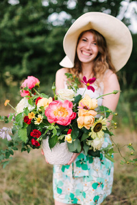婚礼 花艺设计 美容 国家生活概念迷人的草帽和盛大艳丽的牡丹 软黄色雪崩和明亮的红色康乃馨花束的夏装笑女人