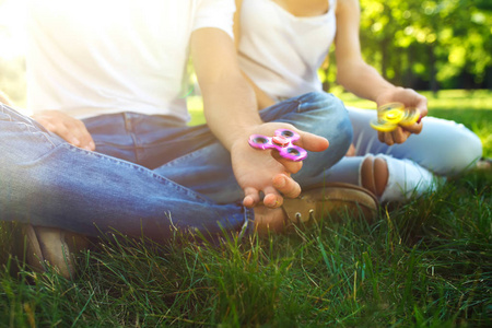 年轻的女孩和男孩坐立不安纺纱在公园里玩。应力解除的玩具。阳光灿烂的夏天的一天。他们笑一笑