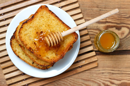 一罐蜂蜜和一把勺子木制背景上的白板上煎烤面包