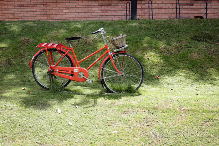 老式红色自行车在绿色的领域与阳光和红砖墙壁在后面的地面