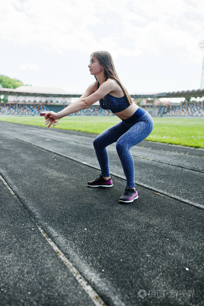 一位漂亮的女生做蹲起动作在体育场的肖像照片-正版