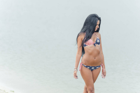 年轻美丽的黑头发女人在水的海滩上摆姿势