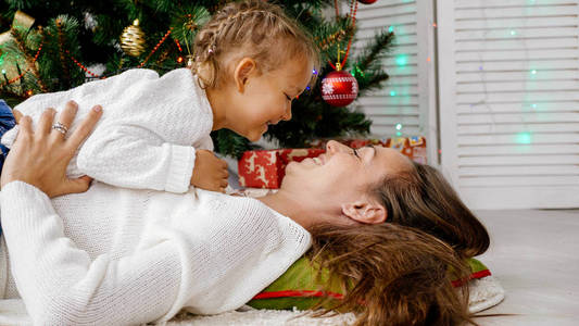 小女孩和妈妈拥抱在室内用圣诞树的背景