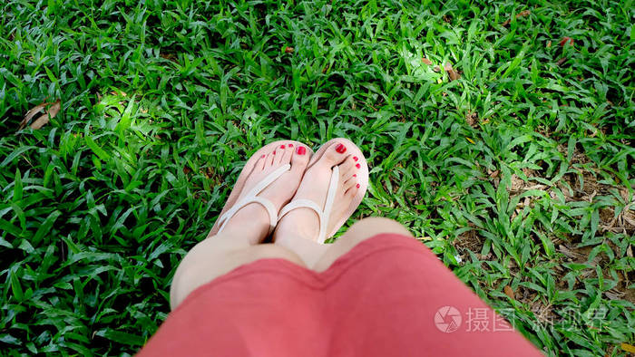 在绿色草地上穿着凉鞋的女孩的脚上特写