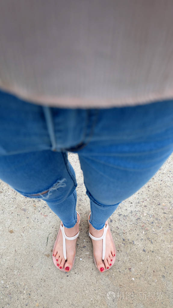 在水泥上穿凉鞋和蓝色牛仔裤的女孩脚上特写