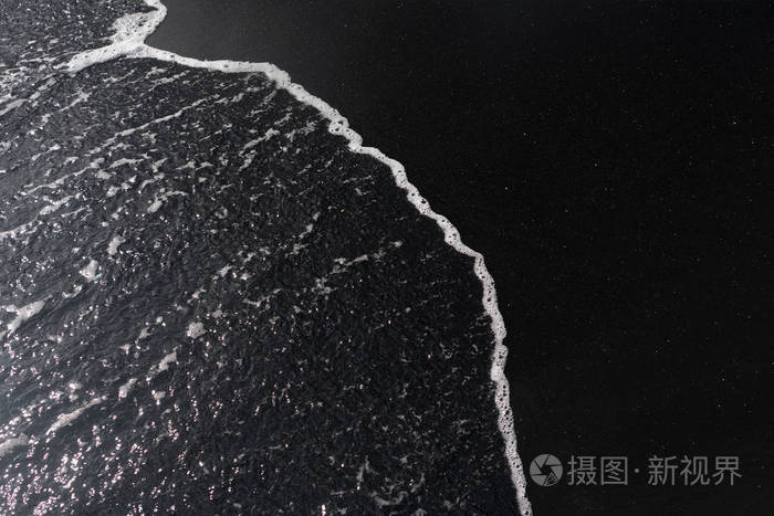 白色的海洋泡沫在黑色的沙子纹理