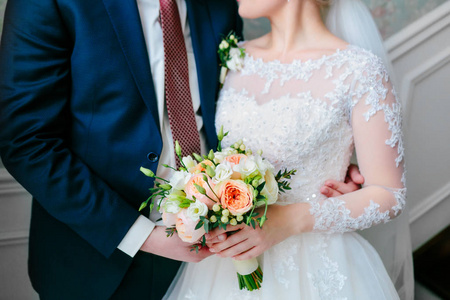 站在房间的白裙子和一套蓝西装的新郎新娘，举行婚礼花束
