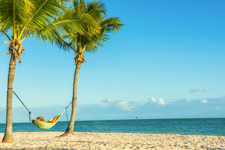 与休息的人在海边沙滩上的两棵棕榈树之间的吊床