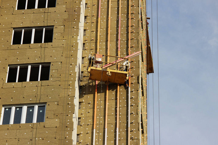 工人在黄色的悬浮摇篮安装在新建的高层建筑的保温环境板