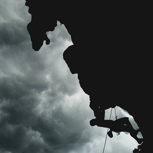 雨云在悬崖上的登山者的剪影图片
