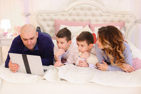 幸福的家庭花时间在一起背后的笔记本电脑，躺在床上