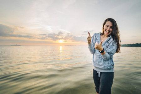 幸福的女人站在沙滩上大拇指与背景的日出