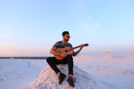 有吸引力的阿拉伯家伙上吉他，坐在山上在唱歌