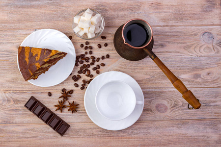 一块巧克力蛋糕上一碟和一杯咖啡 一碗糖多维数据集 咖啡豆 茴香与明亮木制的桌子上的巧克力棒的顶视图