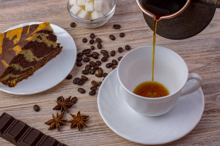 一杯咖啡和茶碟的美味蛋糕。巧克力棒，咖啡豆，方糖，与茴香亮木制背景上的一碗。顶视图