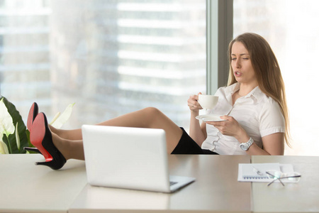 慵懒的轻松女商人上班喝咖啡,脚在桌子上照片