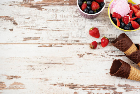 粉红的冰激淋配浆果草莓和蓝莓在一个黄色的碗里。华夫饼的球果，巧克力。光仿古木制背景