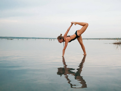 白种人在练习瑜伽中水李曼 湖泊或河流的泳装少妇。美丽的倒影。复杂的体式，平衡。健身 运动 瑜伽和健康的生活方式的概念