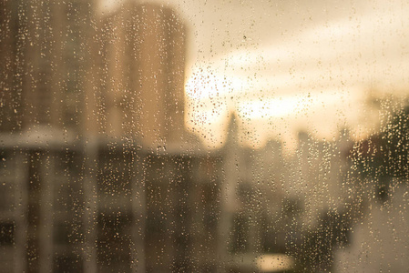 玻璃窗上的雨滴。模糊的建筑物和温暖的色调