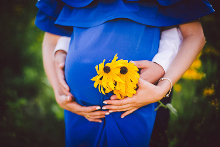 父亲和怀孕母亲与黄色的花朵一起手牵着手在一片绿色的草地上