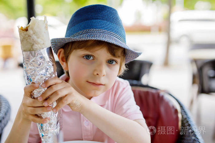 可爱健康的学龄前孩子男孩吃土耳其烤肉串,坐在咖啡馆户外