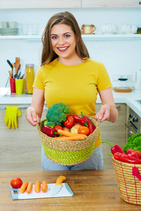 微笑的女人站在厨房里拿着篮子的蔬菜
