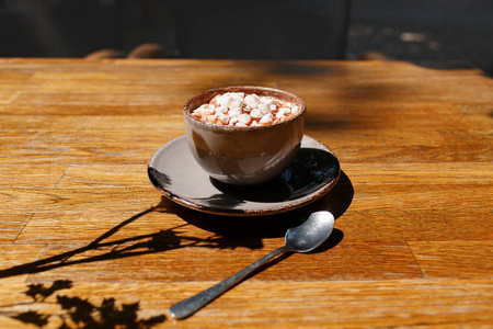 一杯咖啡, 在木桌上的木制桌子的背景。用金属勺子在瓷杯里喝可可饮料