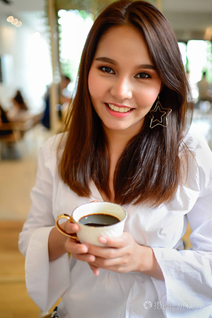 美丽的女人,拿着一杯咖啡在她手中模糊背景咖啡店的画像,她是在早上喝