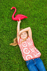 微笑的小女孩躺在绿色的草地上和粉红色的火烈鸟