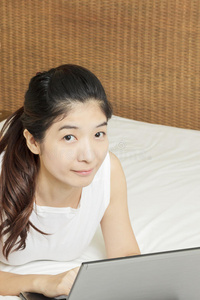 在卧室里用笔记本电脑工作的快乐年轻亚洲女人