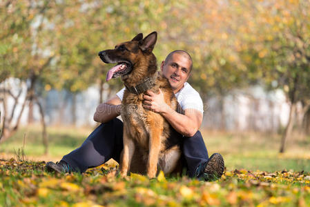 和德国牧羊犬一起坐在户外的成年男子