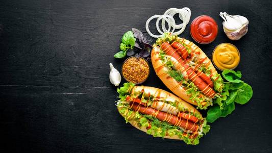 热狗与烤的香肠 芥末和番茄酱，洋葱和青菜上木制的背景。顶视图。可用空间