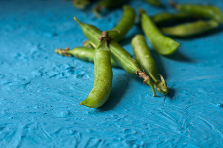 年轻的有机绿色豌豆荚和豌豆在蓝色纹理的背景。关闭。收获，健康饮食