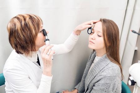 检查在私人诊所的年轻女人眼睛的高级女性验光师