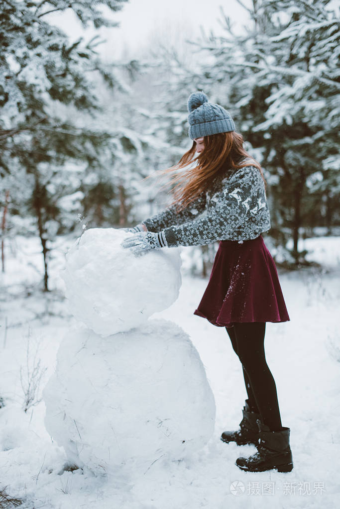 时髦女孩开心,雪人在冬季时间森林,穿着毛衣和围巾,在户外,下雪的天气