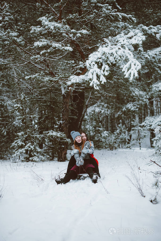 关闭了的两个姐妹拥抱时尚肖像和最好的朋友开心,骑雪橇在冬季时间