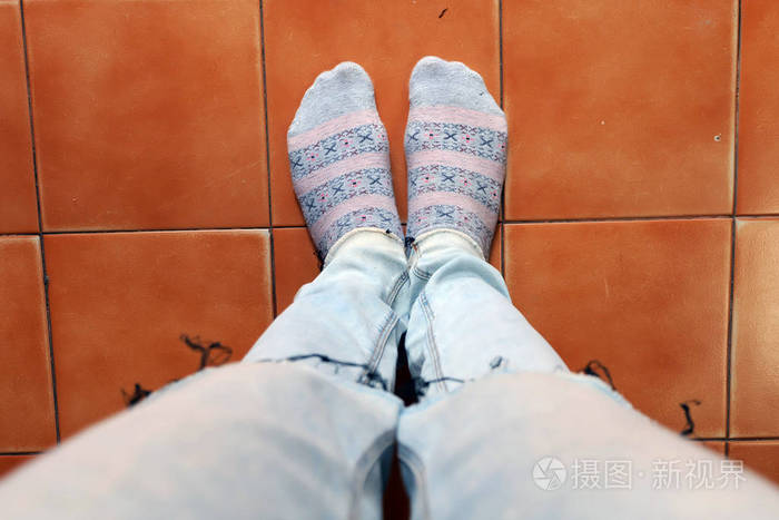 近距离女性的脚穿袜子和蓝色牛仔裤在棕色瓷砖背景