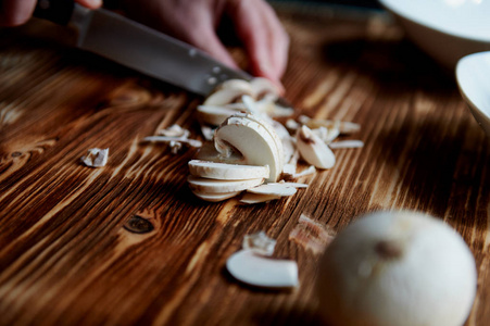 人们用刀切蘑菇。切片是相邻的。木质的表面