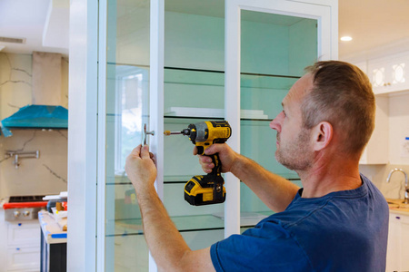 橱柜安装工人用螺丝刀在白色柜子上装上一个新把手,安装厨房橱柜照片