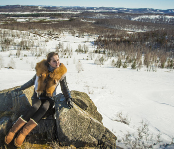 穿黑色外套的年轻女人，戴着狐狸姜毛领子摆姿势。 冬季和山区景观。