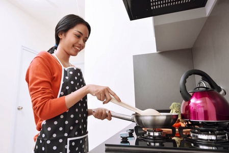 微笑亚洲女人使用煎锅和烹饪