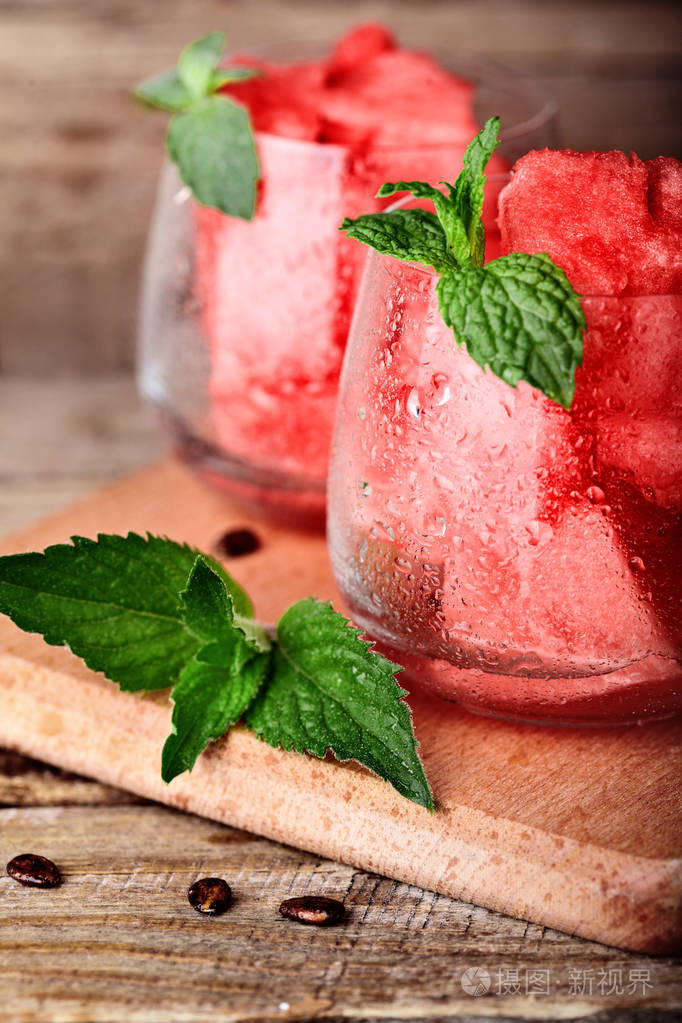 西瓜切成小块在备选方案与水滴装饰着薄荷仿古木制的桌子上.