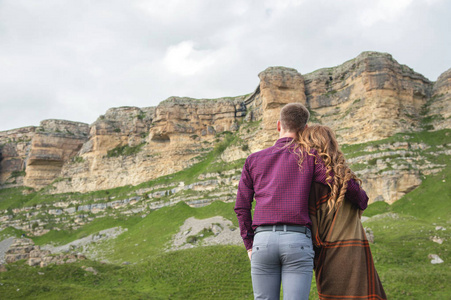 一个男人和一个女孩的画像覆盖在地毯上站着，背在大自然的怀抱中，看着岩石