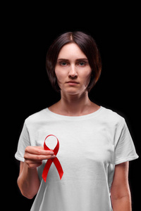年轻的严重女子捧红丝带着黑色的背景上。艾滋病的认识。健康意识概念