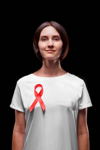 与艾滋病人的团结。微笑的女性，在黑色背景上的一件 t 恤上的红丝带。健康意识概念