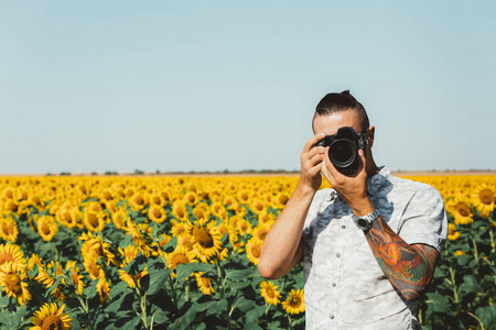 男摄影师用相机照片制作在户外对向日葵场手中的画像
