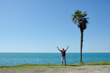 与他举起手来在海洋和蓝色天空的背景上的高大的棕榈树站在一起的人